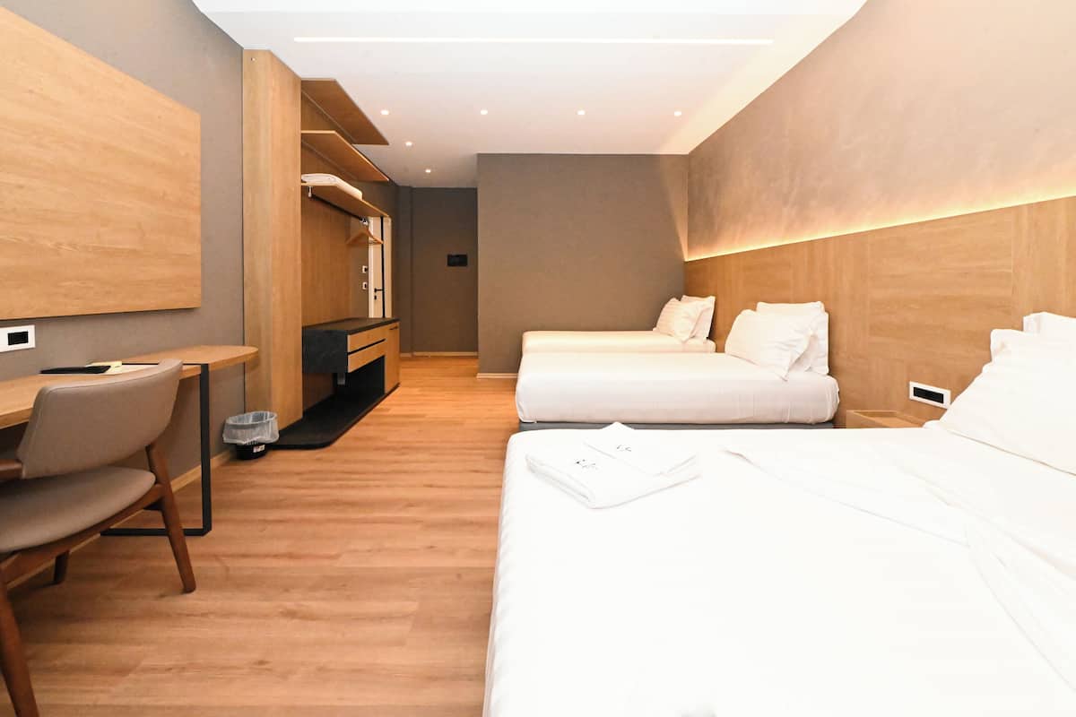 A modern hotel room with a wooden floor, a desk with a chair, two beds, and a wardrobe.