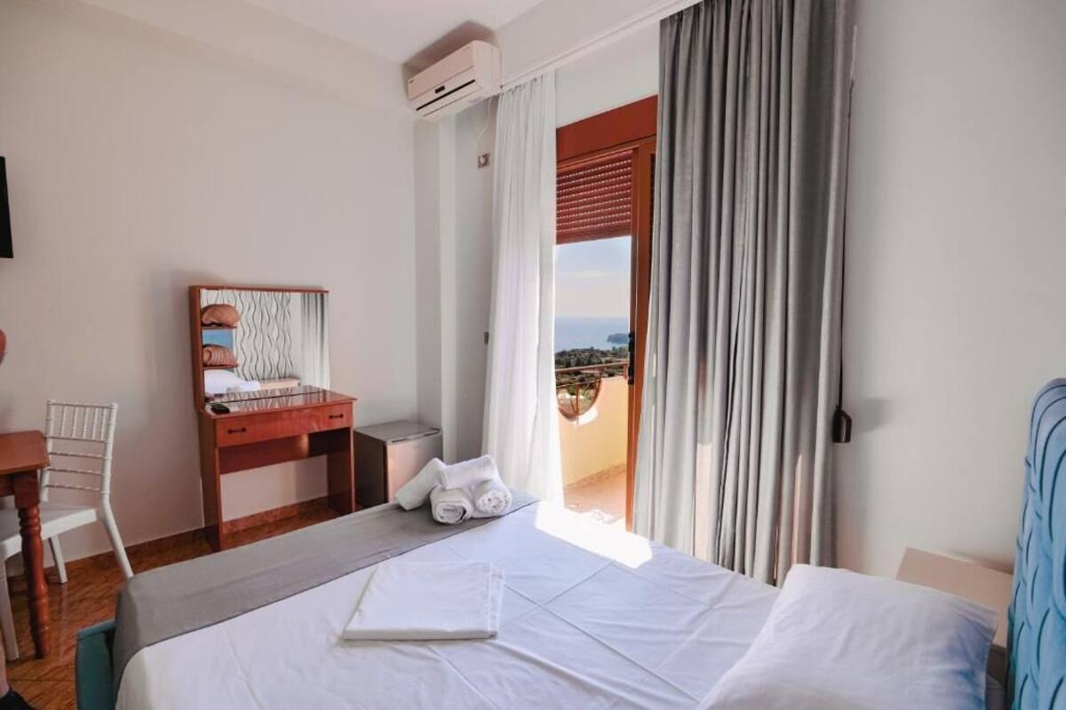 A hotel room with a bed, a desk with a chair, a window with curtains, and a view of the outside.