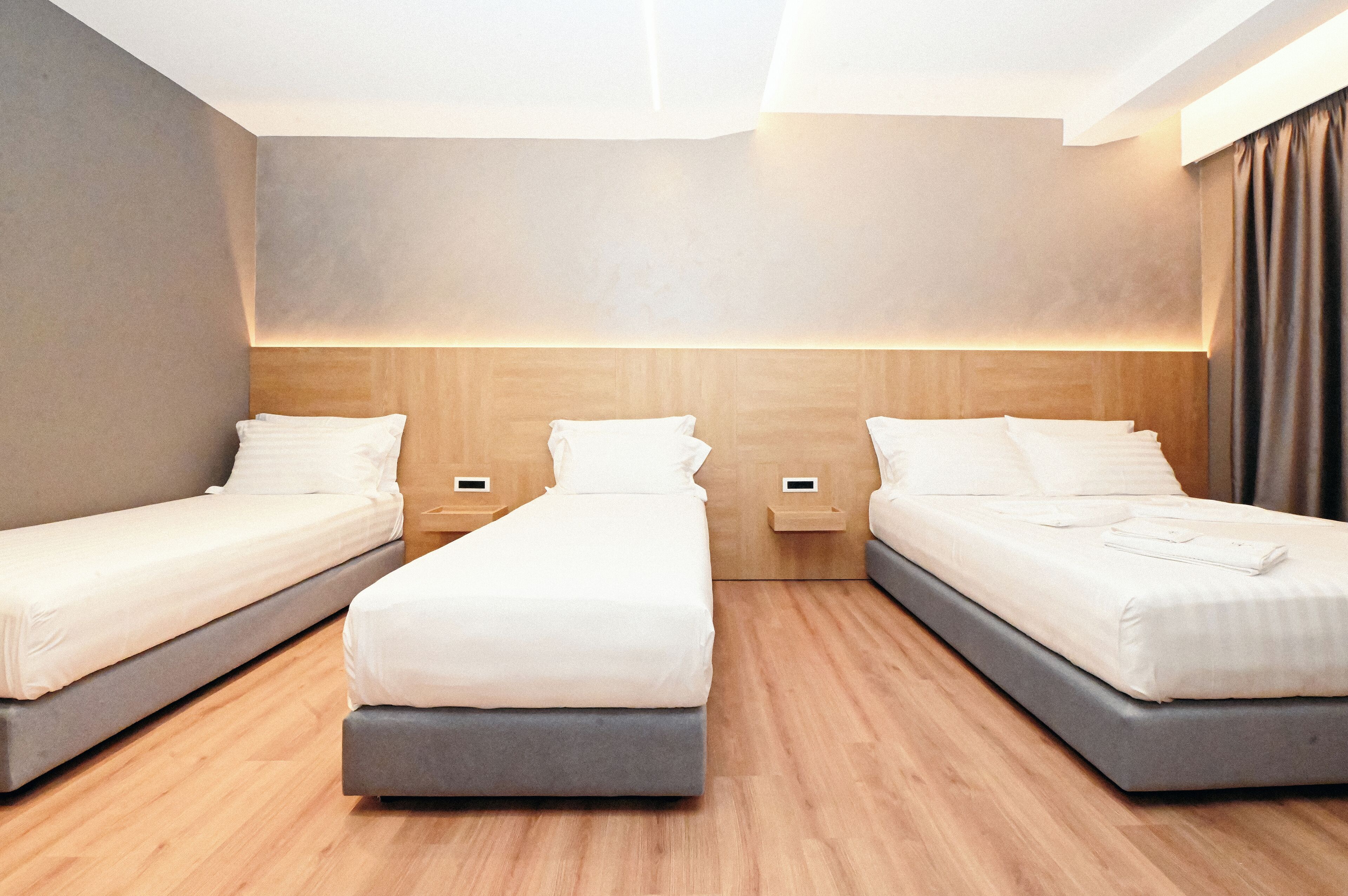 A modern hotel room with two single beds, a large bed, wooden flooring, and a neutral color scheme.