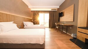 A hotel room with two beds, a desk, a TV, and a large window with curtains. - Hotel Panorama (Himarë)