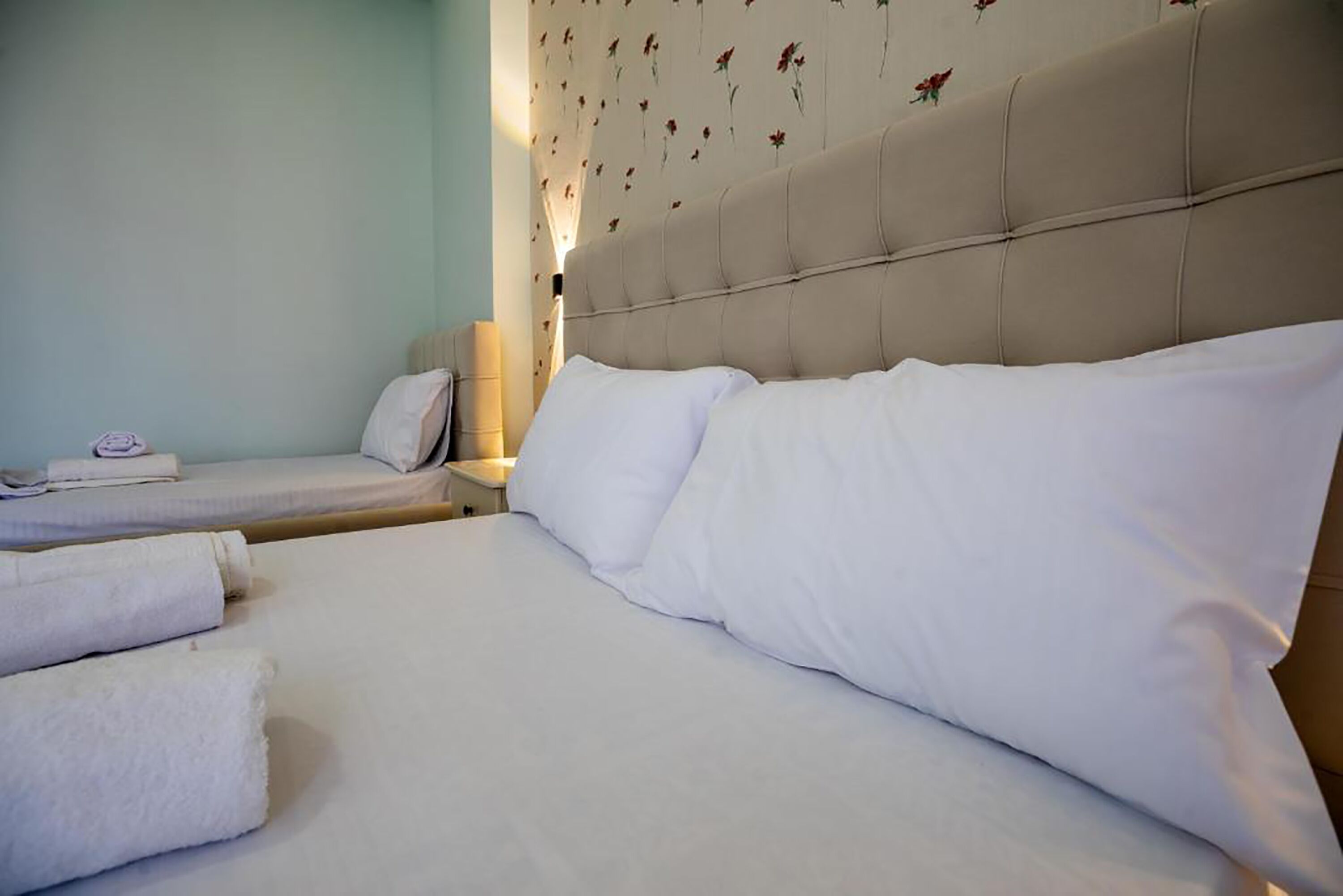 Hotellihuone, jossa on suuri sänky, pienempi sänky ja yöpöytä, jossa on lamppu.