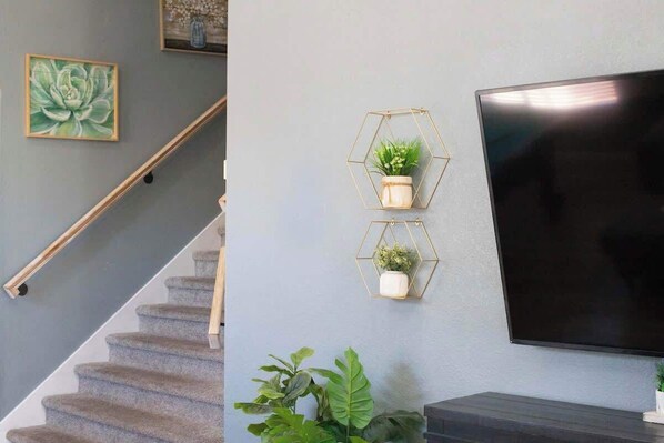 A staircase with a wooden handrail, a wall-mounted TV, and two hexagonal wall sconces with plants.