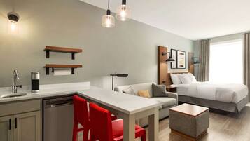 A modern hotel room with a kitchenette, a bed, a sofa, and a dining area.