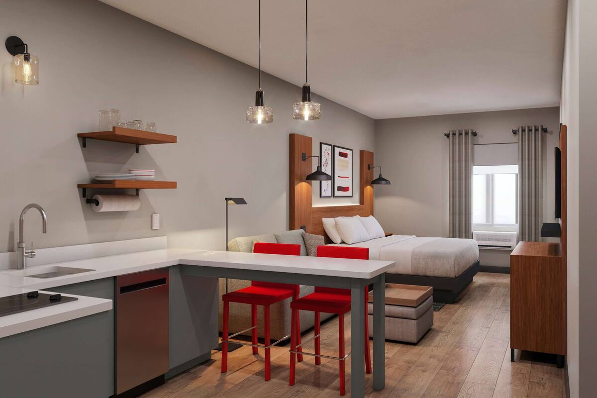 Una habitación de hotel moderna con kitchenette, una cama, una zona de estar y un televisor.
