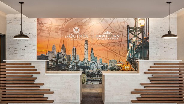 Un área de recepción con un mural de la ciudad, listones de madera e iluminación colgante.