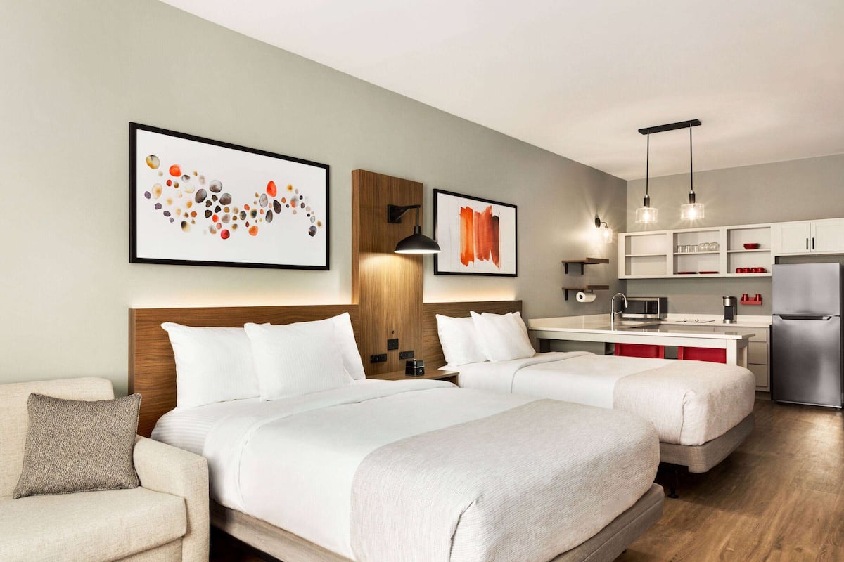 Una habitación de hotel con dos camas, una kitchenette y obras de arte en las paredes.