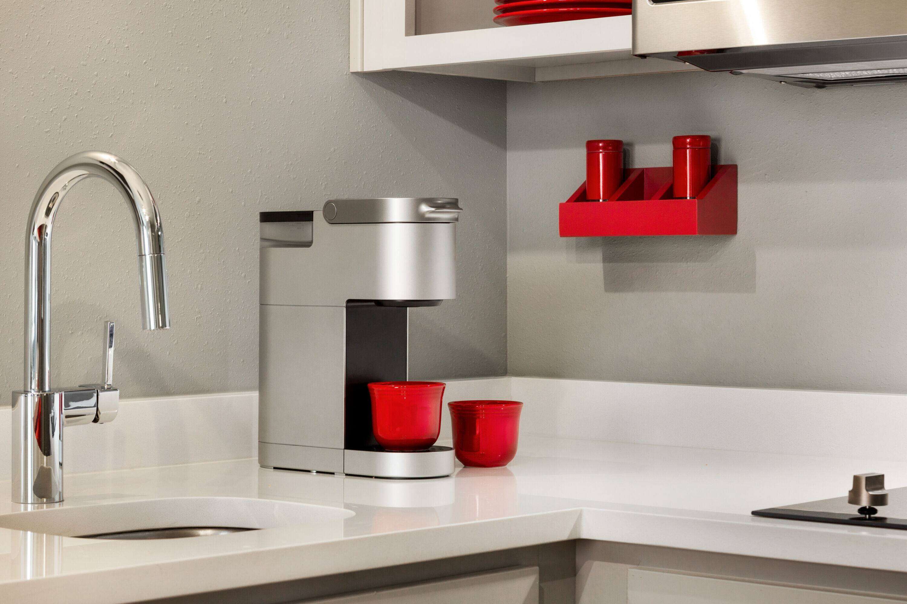 A modern kitchen with a stainless steel sink, a coffee maker, and red cups on the counter.