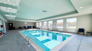 Una amplia piscina cubierta con carriles delimitados, suelo de baldosas y ventanas con vistas al exterior.