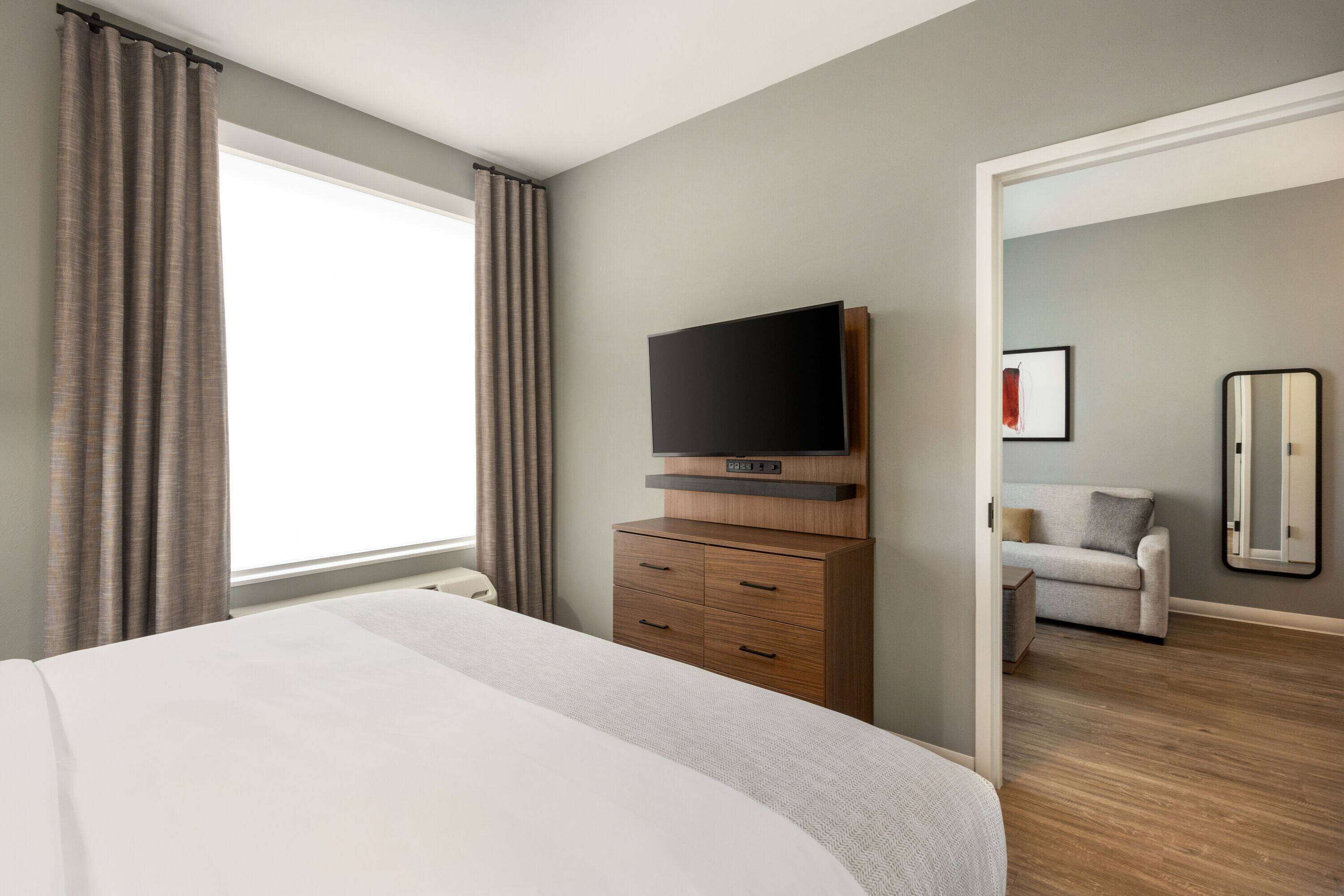Quarto de hotel com cama grande, televisão de tela plana em cômoda de madeira, sofá e espelho.
