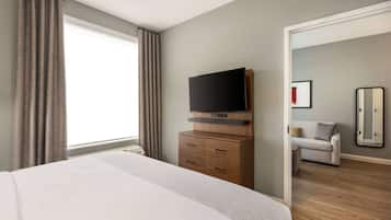 Quarto de hotel com cama grande, televisão de tela plana em cômoda de madeira, sofá e espelho.
