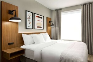 Habitación de hotel con una cama grande, dos lámparas de lectura fijadas a la pared y un ventanal con cortinas.