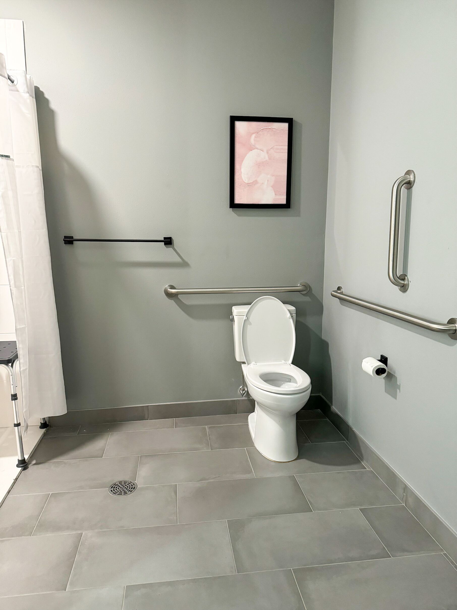 Une salle de bain moderne équipée de toilettes, de barres d’appui et d’un espace douche.