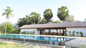 A poolside view of a building with a covered patio and palm trees.