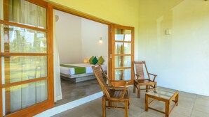 A room with a bed, two wooden chairs, a glass table, and large windows with curtains.