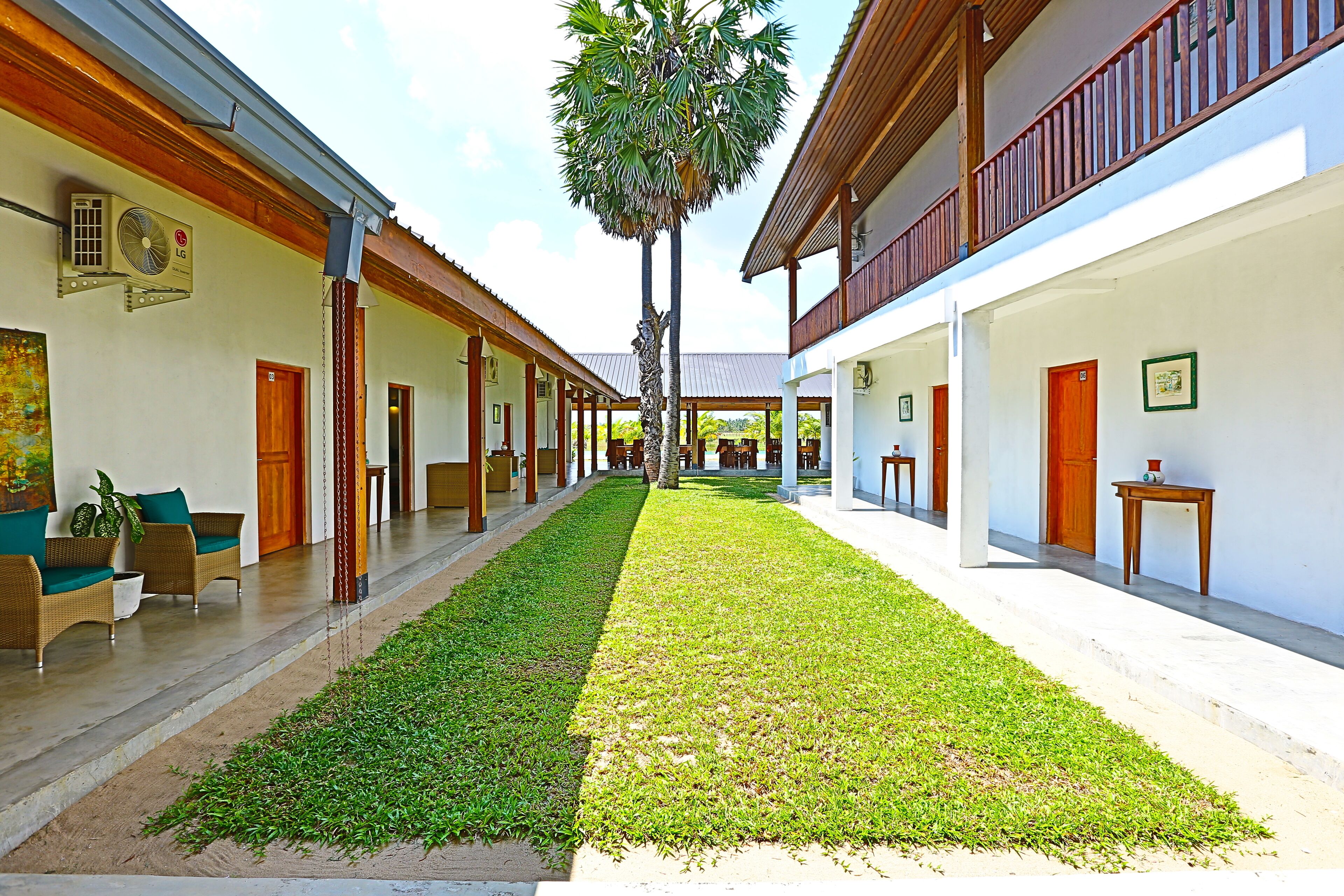 A corridor with a central lawn, wooden benches, and a palm tree.
