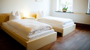 A bedroom with two single beds, wooden headboards, white bedding, bedside tables with lamps, a window with a view of the outside, and a radiator. - Tillas Hof (Hamm)