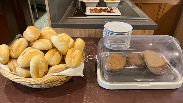 A buffet table with a basket of bread rolls and a container of sliced bread. - Tillas Hof (Hamm)