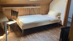 A small, cozy bedroom with a sloped ceiling, a skylight, a bed, a chair, a desk, and a television. - Tillas Hof (Hamm)
