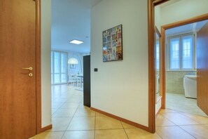Un pasillo con puerta de madera, suelo de baldosas, un cuadro en la pared y una ventana.