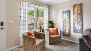 Un salon avec deux fauteuils à motifs, une table basse et une lampe. Deux tableaux abstraits sont accrochés au mur.