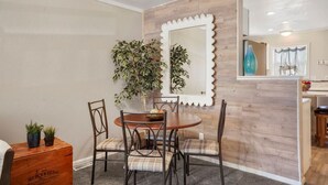 Un coin repas avec une table ronde, quatre chaises, une plante en pot et un miroir décoratif accroché au mur.