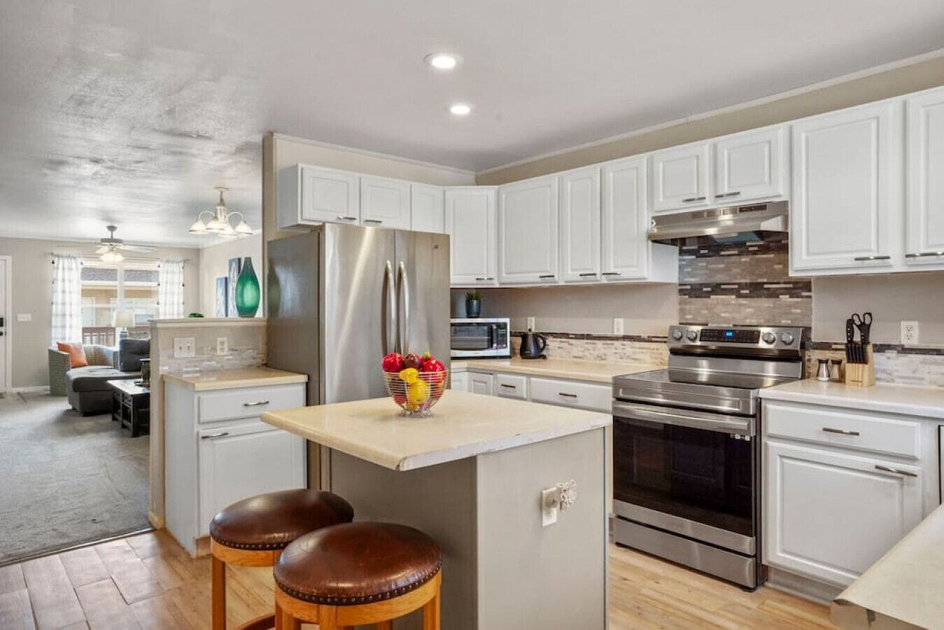 A modern kitchen with white cabinets, stainless steel appliances, and a central island with stools.