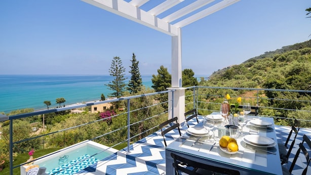 Eine Terrasse mit Esstisch, mit Blick auf die Küste und Hügellandschaft.