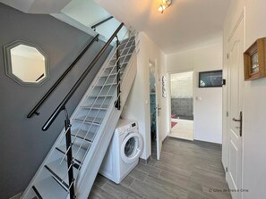 A laundry room with a washing machine, a drying rack, and a staircase with a handrail.