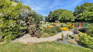 A garden with a variety of plants, a small bridge, and a fountain.