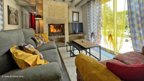 A cozy living room with a fireplace, a sofa, a television, and a large window with curtains.