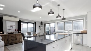 A modern kitchen with a large island, pendant lights, and a view of the outdoors. - Happy Tails Devonport (East Devonport)