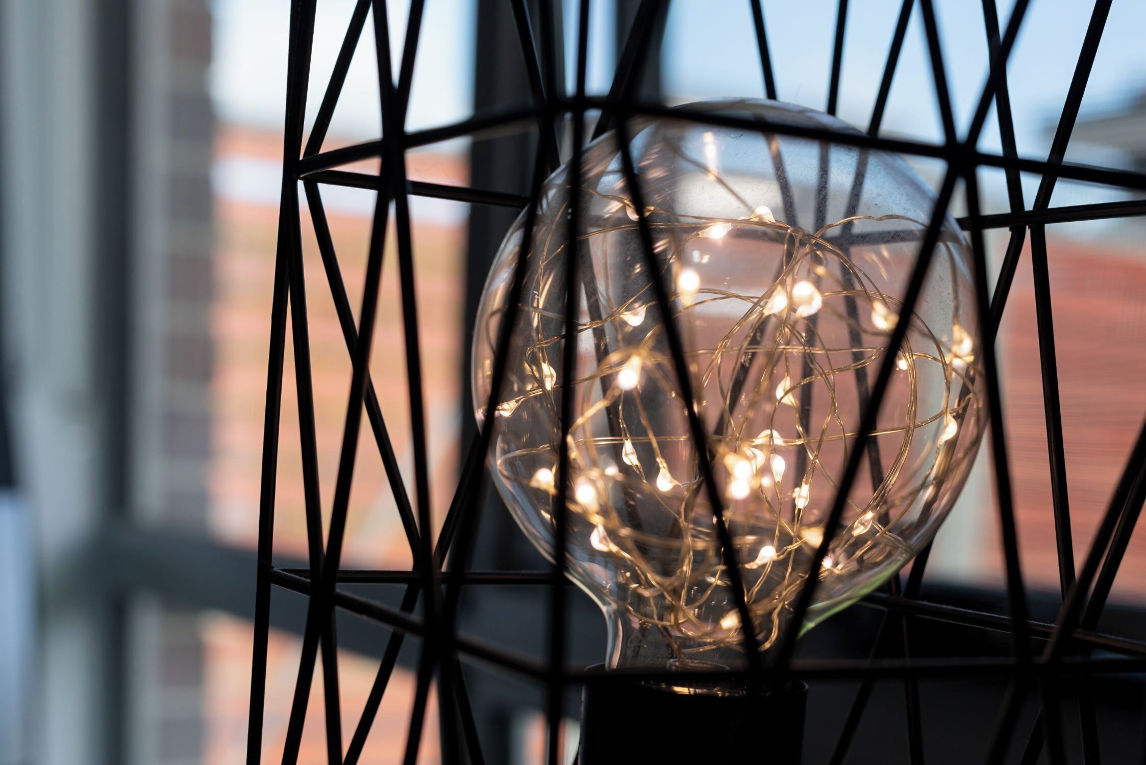 Una lámpara esférica con hilos de bombillas, dentro de una estructura metálica geométrica.