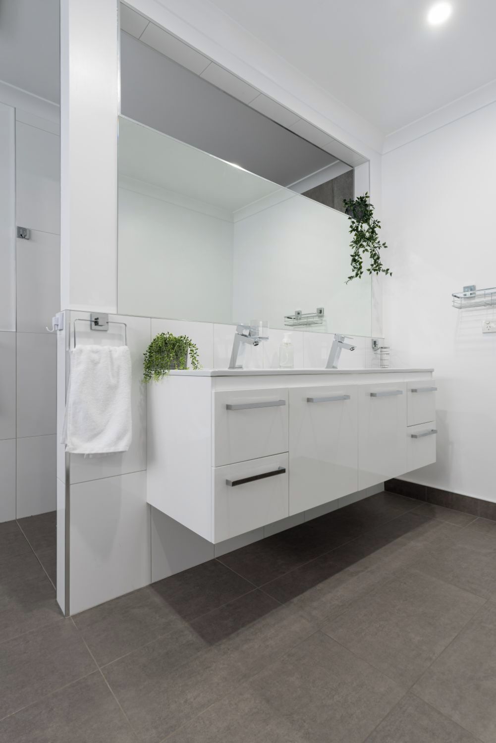 Une salle de bain moderne avec un meuble-lavabo blanc, un grand miroir et une plante posée sur le plan de travail.
