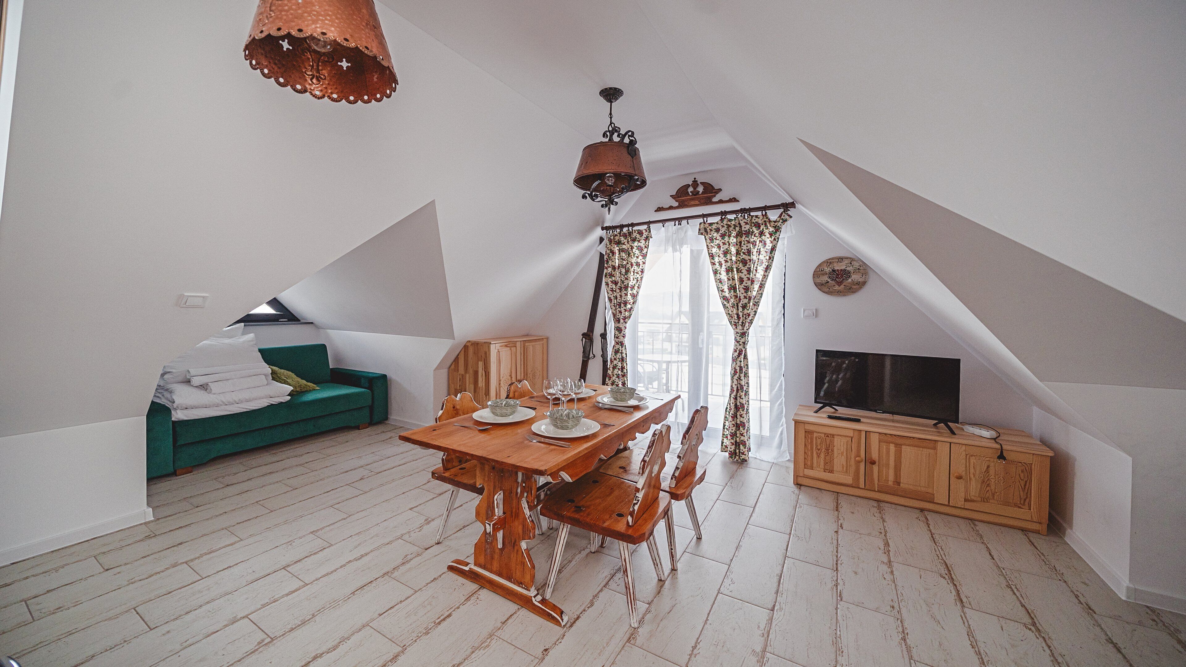 A cozy loft bedroom with a dining area, a green sofa, and a TV.