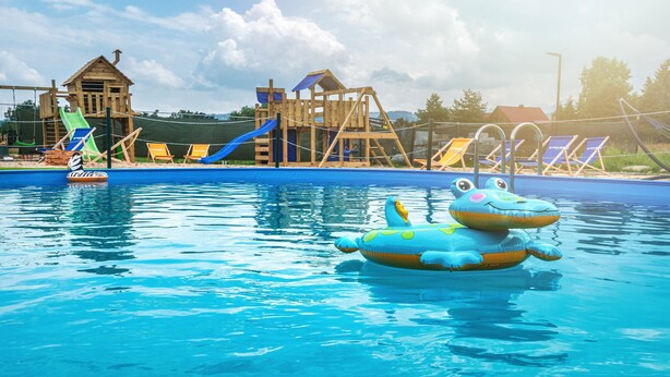 A swimming pool with inflatable toys, a wooden play structure, and lounge chairs.