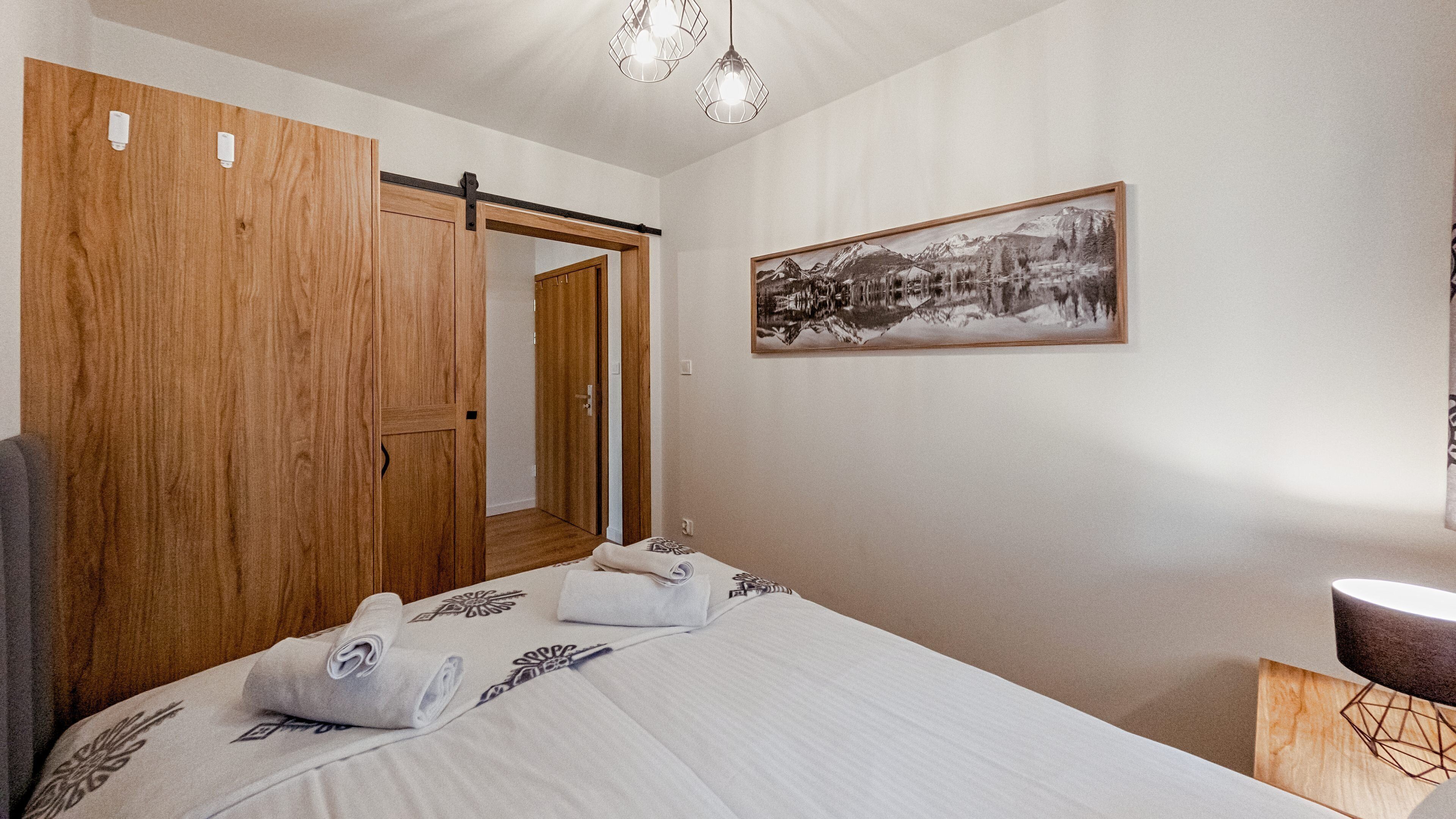 Un dormitorio con un amplio armario de madera, una cama con toallas, un cuadro enmarcado en la pared y una mesita de noche.