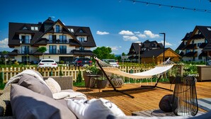 A wooden deck with a hammock and wicker furniture, overlooking a row of houses.