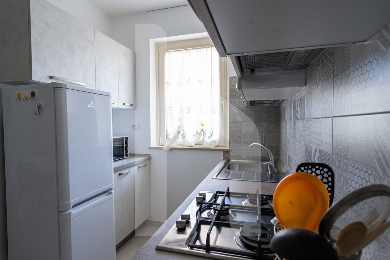 Una cocina con refrigerador, estufa, lavaplatos y ventana con cortinas.