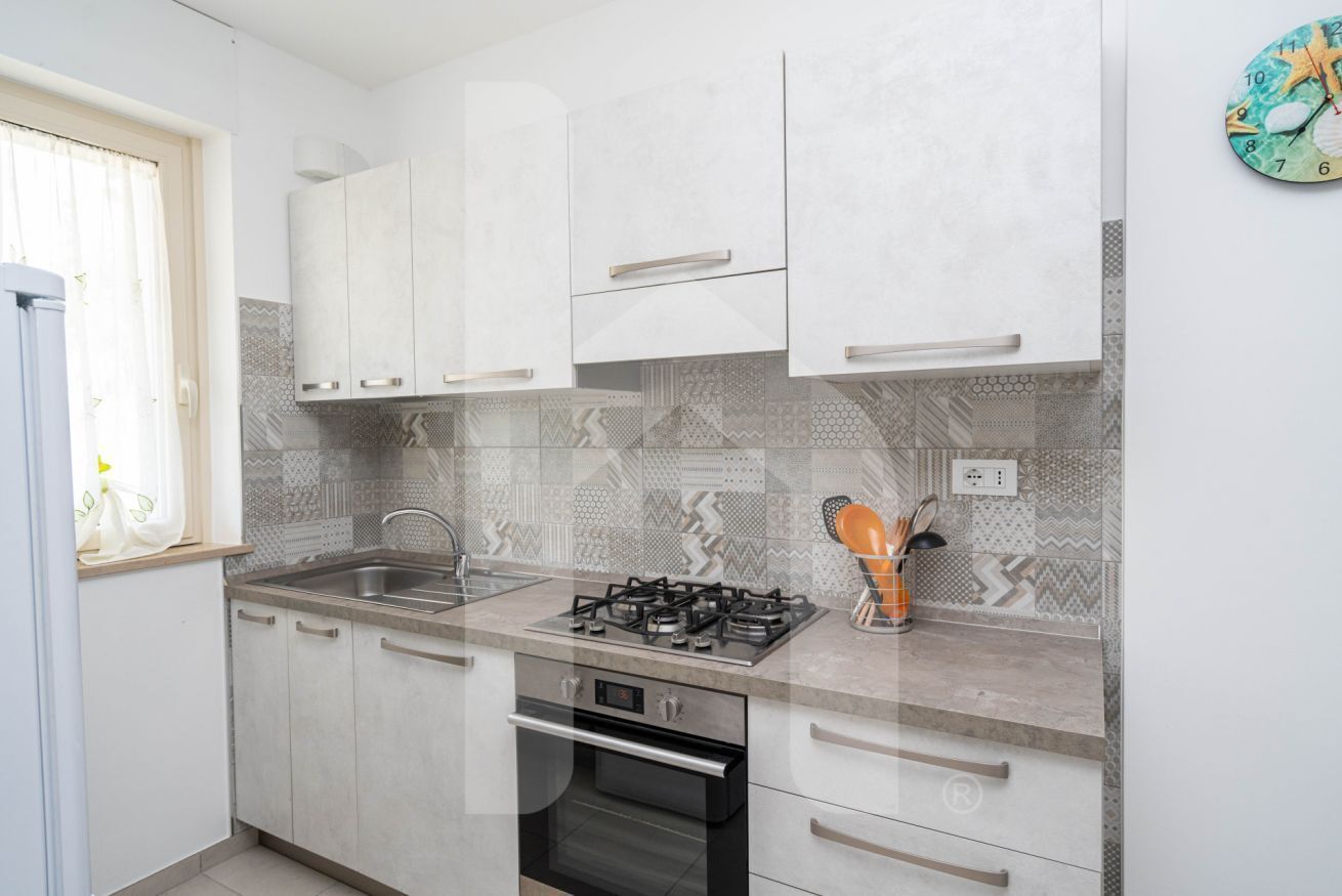 A compact kitchen with white cabinets, a gas stove, a sink, and patterned backsplash tiles.