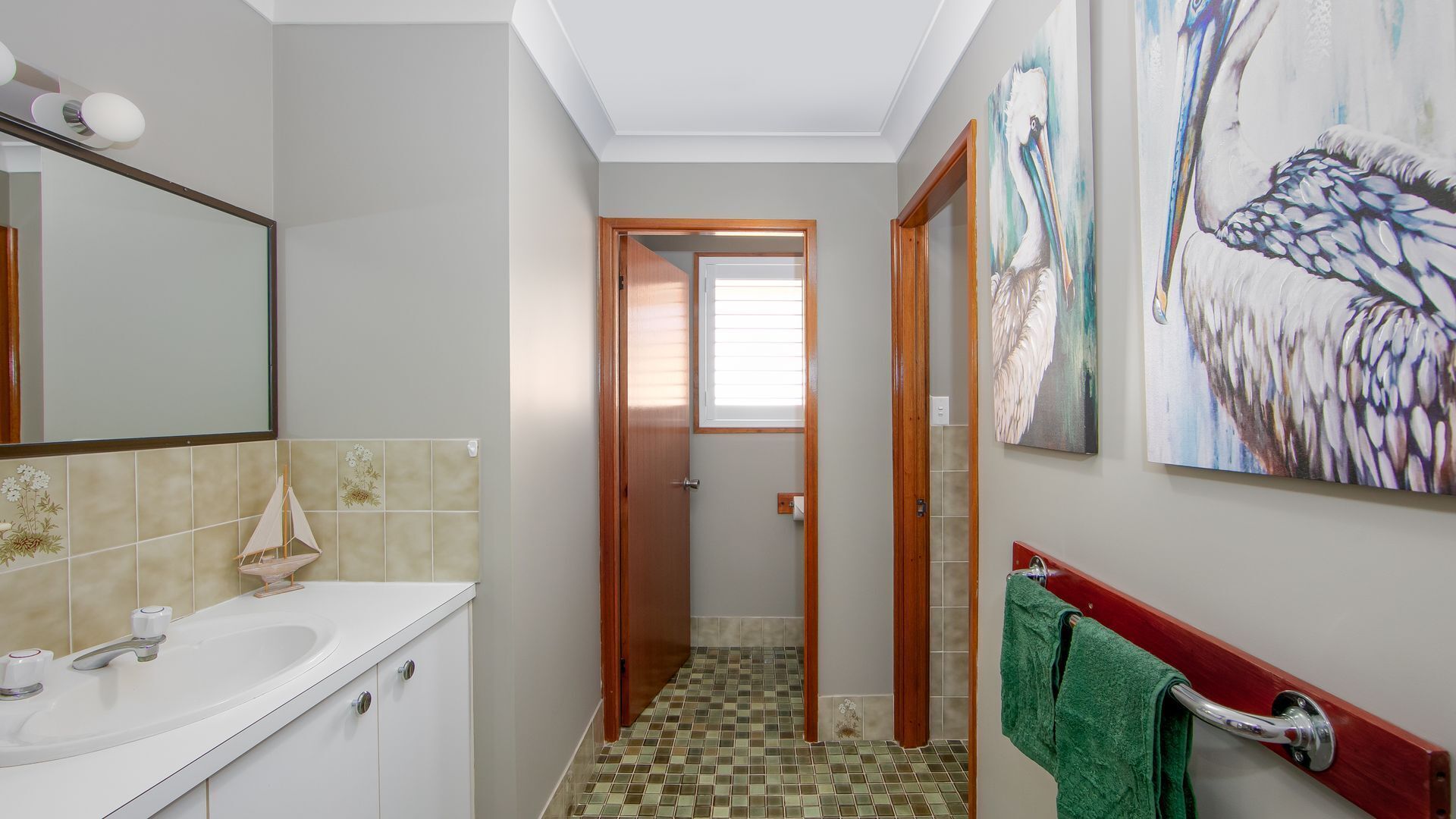 A bathroom with a white sink, a mirror, and a tiled floor. There is a green towel hanging on a rack.