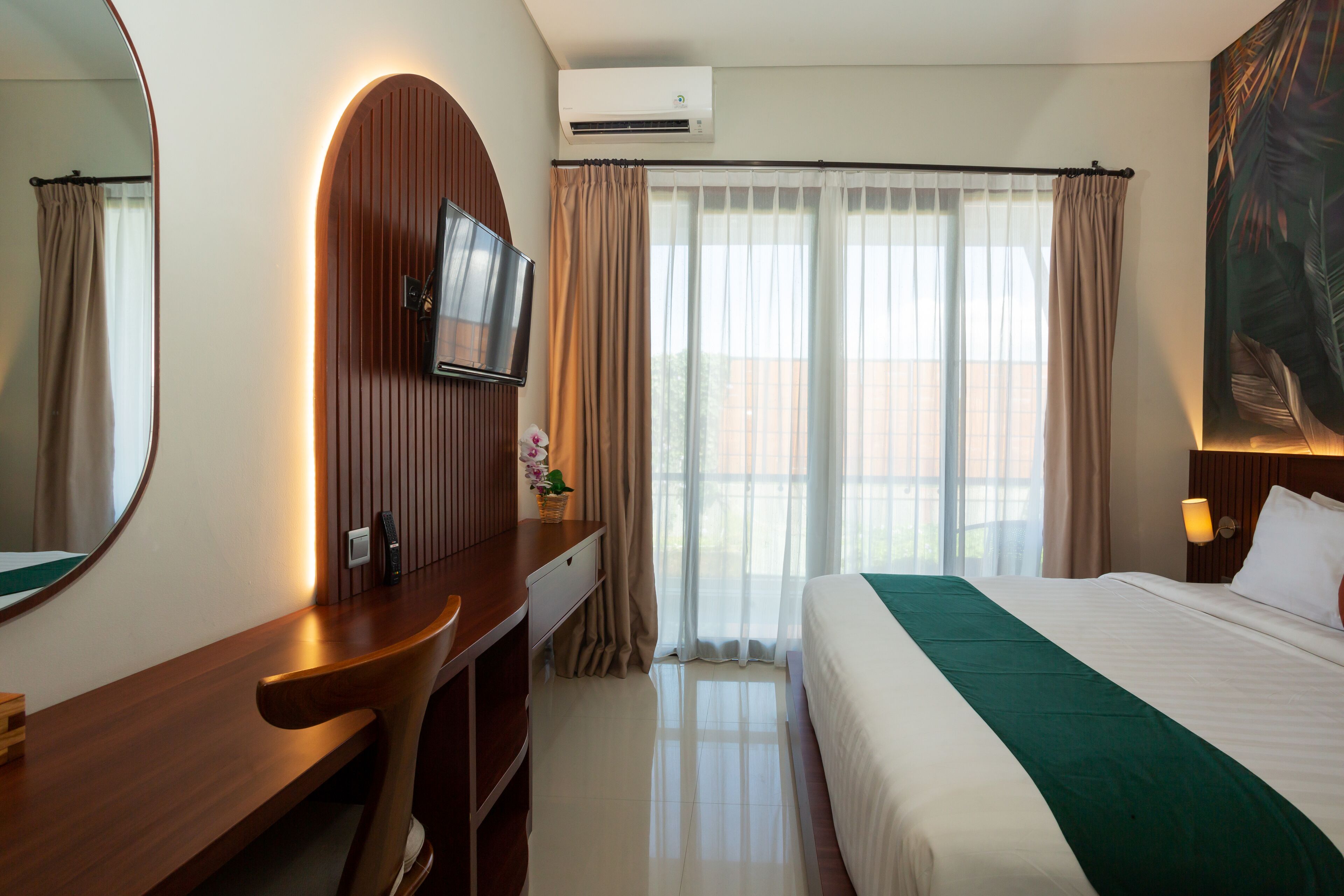 A hotel room with a bed, a desk with a chair, a television, and a large window with curtains.