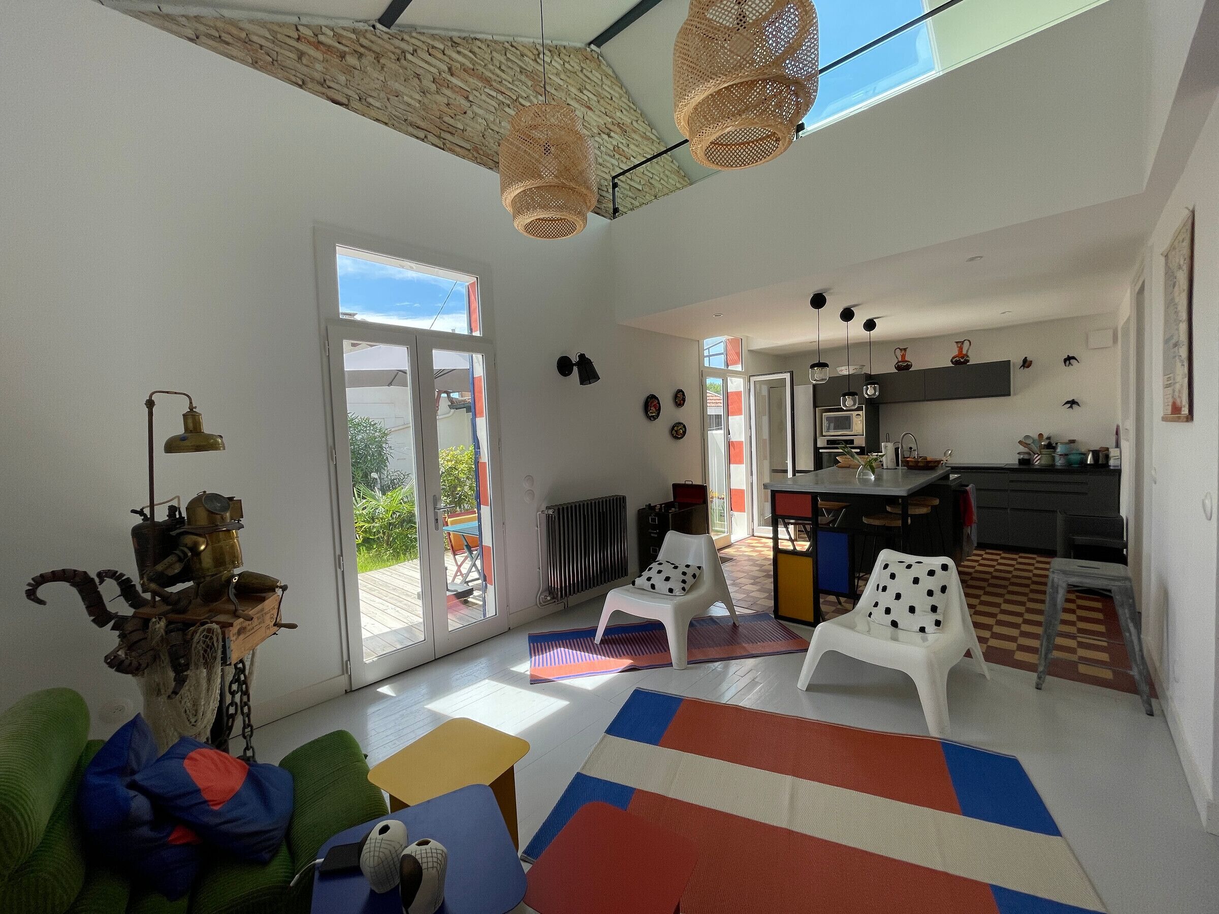 A modern living room with a large window, a kitchen area, and a dining space.