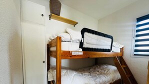 A bunk bed with a wooden frame, white bedding, and a small shelf above it.