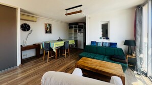 A living room with a wooden floor, a green sofa, a wooden coffee table, and a dining area with a table and chairs.