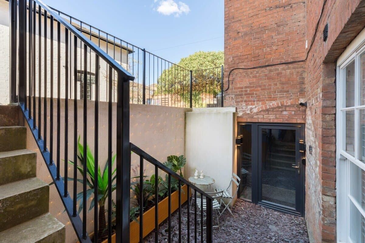 A courtyard with a brick building, a black door, and a staircase with metal railings.