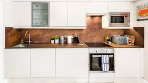 Una cucina moderna con mobili bianchi, un lavandino in acciaio inossidabile, un forno a microonde e un forno da incasso.