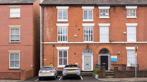A two-story brick house with a front door, two cars parked in the driveway, and a number '70' on the door. - Ground floor compact studio with mini kitchen (Warrington)