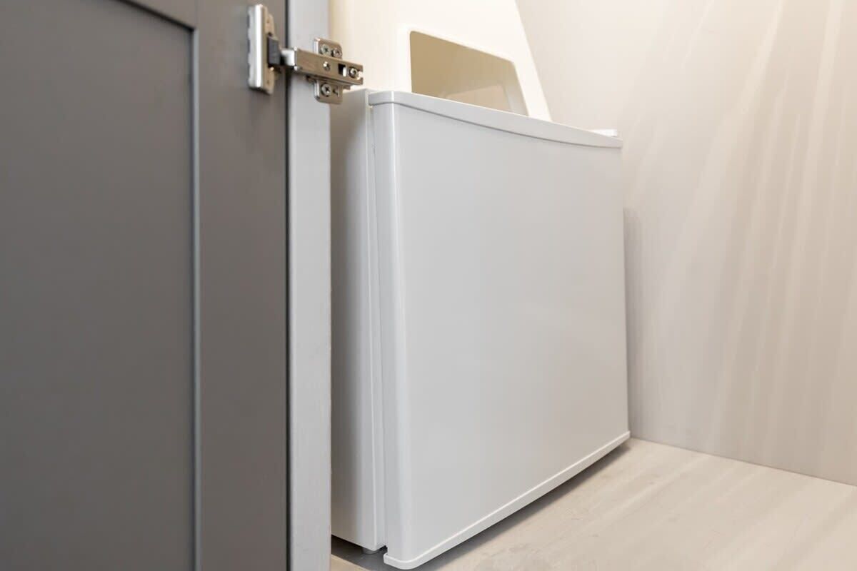 Un radiateur blanc, placé dans un coin d’une pièce, avec une porte grise et un plancher de couleur claire.