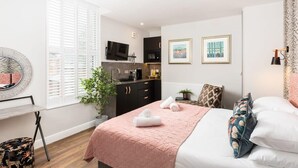 A modern bedroom with a bed, a bedside table, a potted plant, and a view of a kitchen. - First floor compact studio with kitchenette (Warrington)
