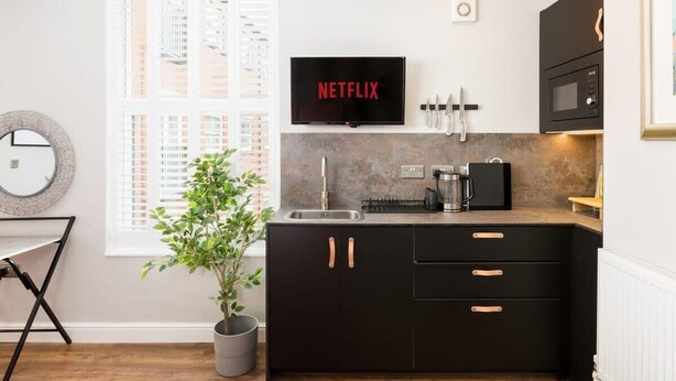 A modern kitchen with a black countertop, a sink, and a mounted television displaying "NETFLIX". - First floor compact studio with kitchenette (Warrington)